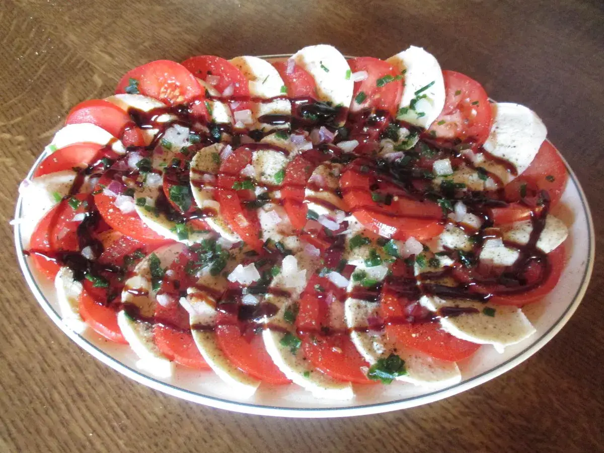 Tomaten-Mozzarella-Salat mit Balsamico-Dressing, garniert mit Zwiebeln und Kräutern. Ein köstlicher und erfrischender Salat.