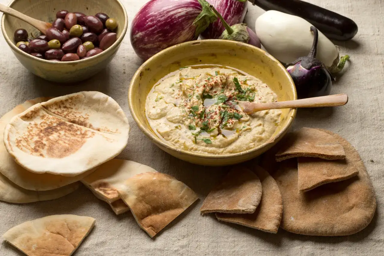 En skål med krämig baba ganoush, pitabröd, oliver och auberginer. Perfekt för ett baba ganoush recept.