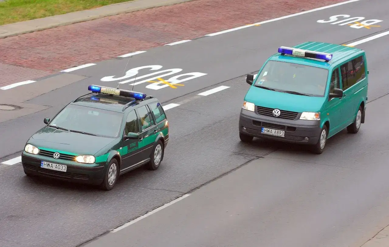 Dwa pojazdy Straży Granicznej, w tym kombi i van, z włączonymi niebieskimi światłami, jadące na kursie pojazdy uprzywilejowane.