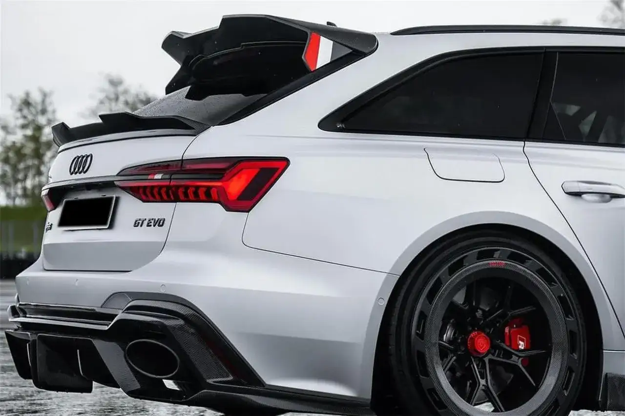 Białe Audi RS6 GT z masywnym spojlerem i dyfuzorem z włókna węglowego. Widoczne czerwone zaciski hamulcowe i unikalne felgi.