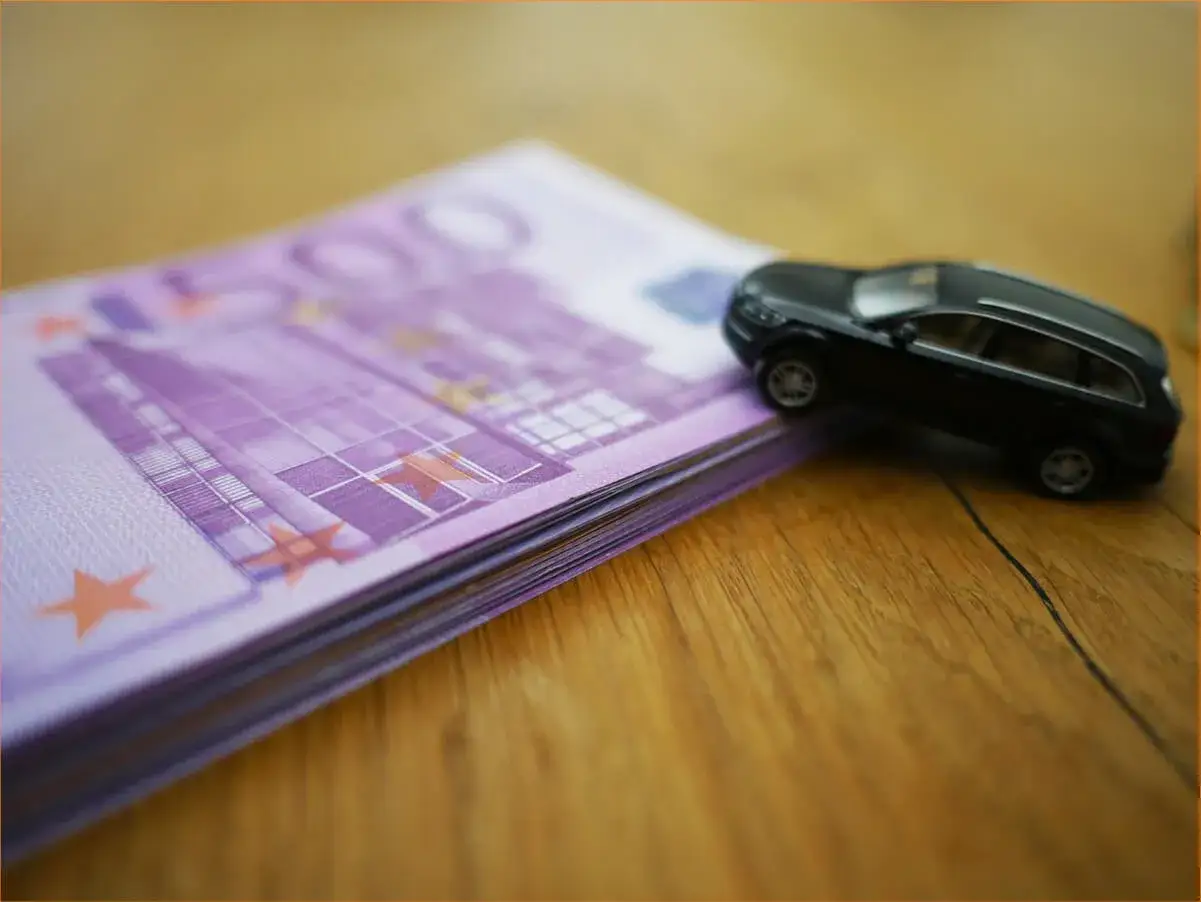 Czarny model samochodu na stosie banknotów 500 euro na drewnianym tle.