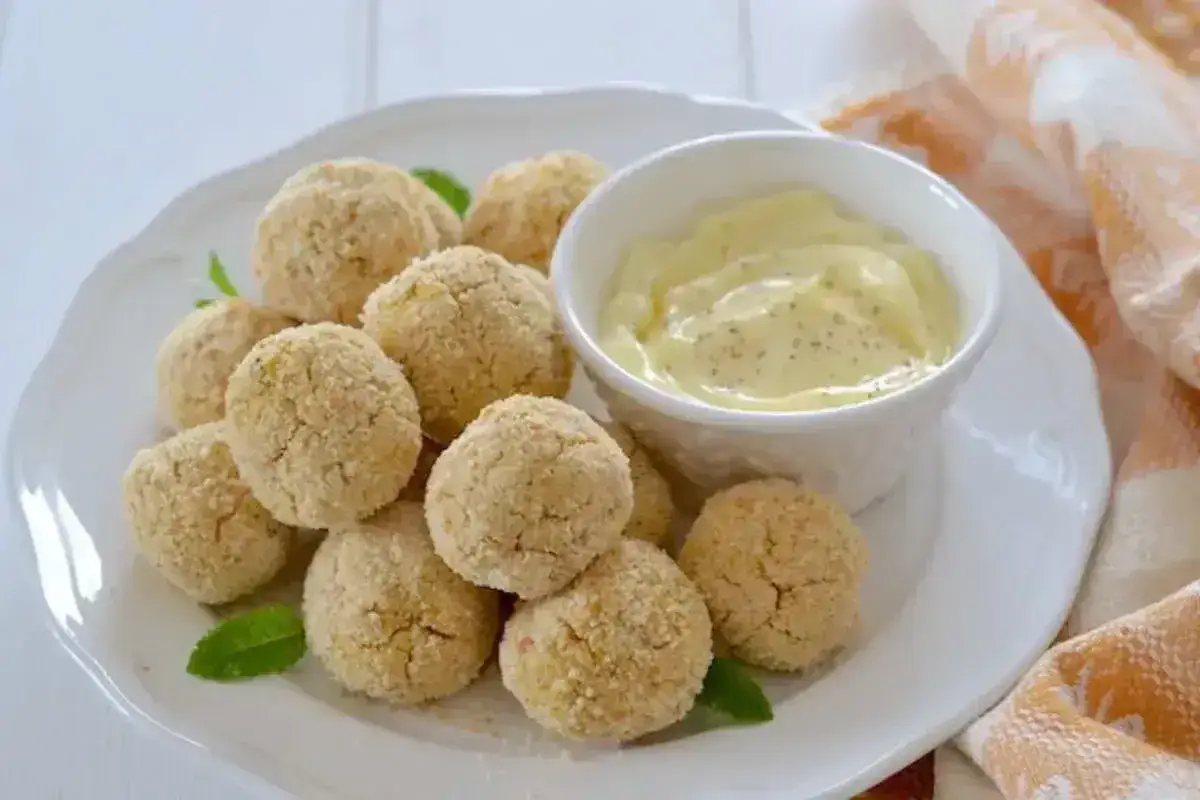Polpette al forno dorate e croccanti, servite con una cremosa salsa gialla e foglie di menta fresca.