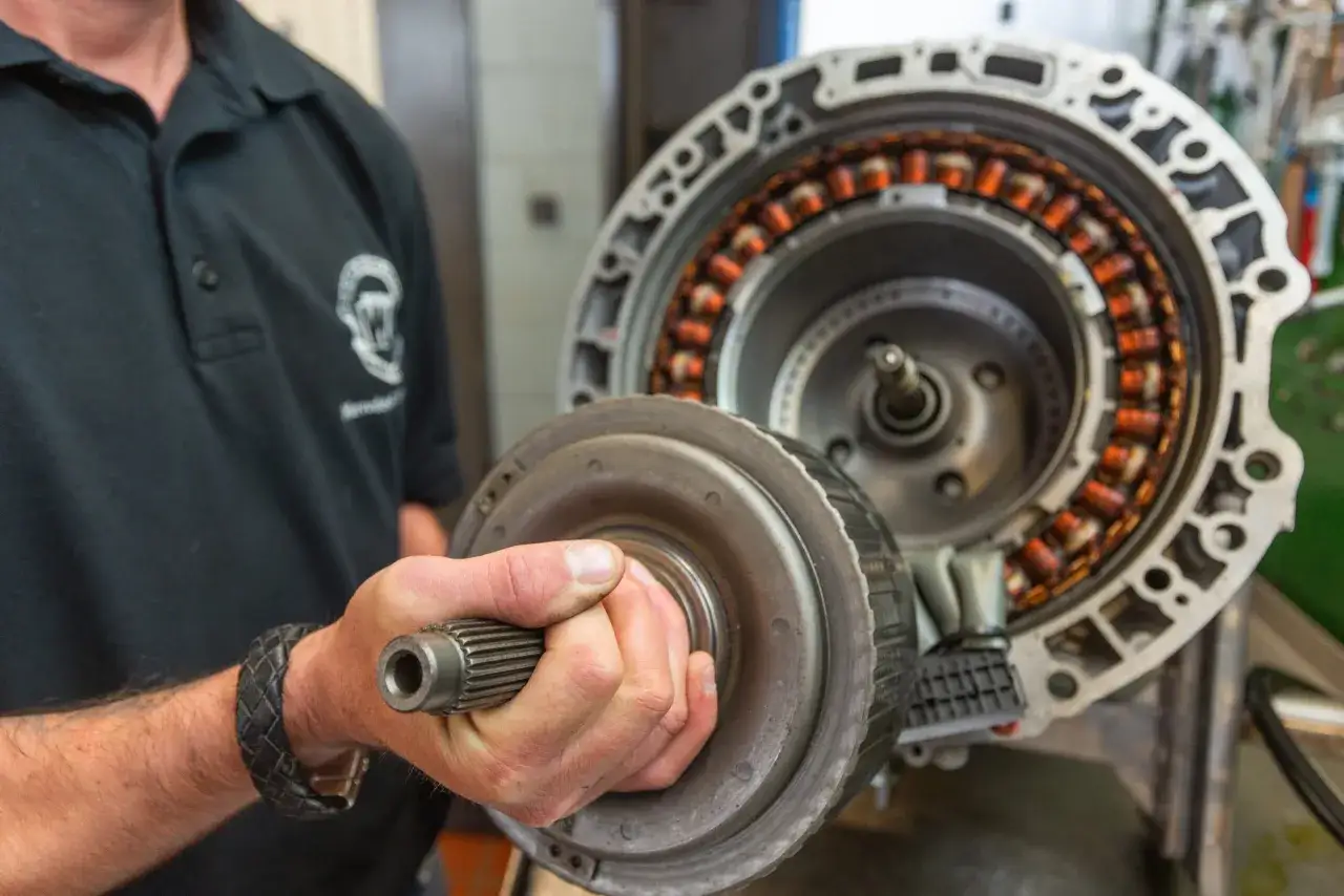 Mechaniker hält Drehmomentwandler vor offenem Getriebe. Informieren Sie sich über die getriebe wechseln kosten.