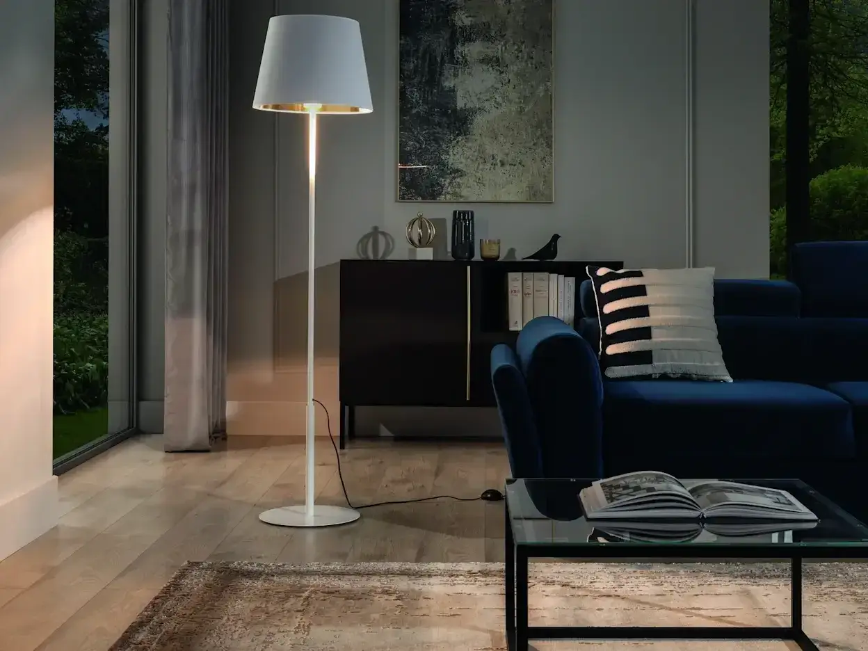 Eleganckie lampy stojące do salonu oświetlają przytulne wnętrze z granatową kanapą i szklanym stolikiem.