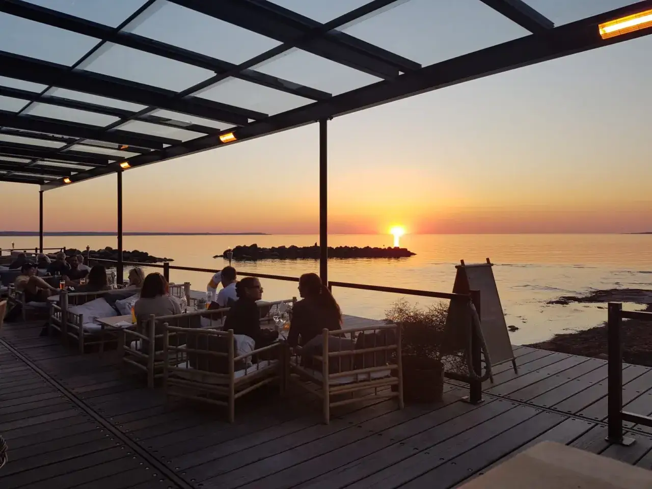 En restaurang vid havet med gäster som njuter av solnedgången.