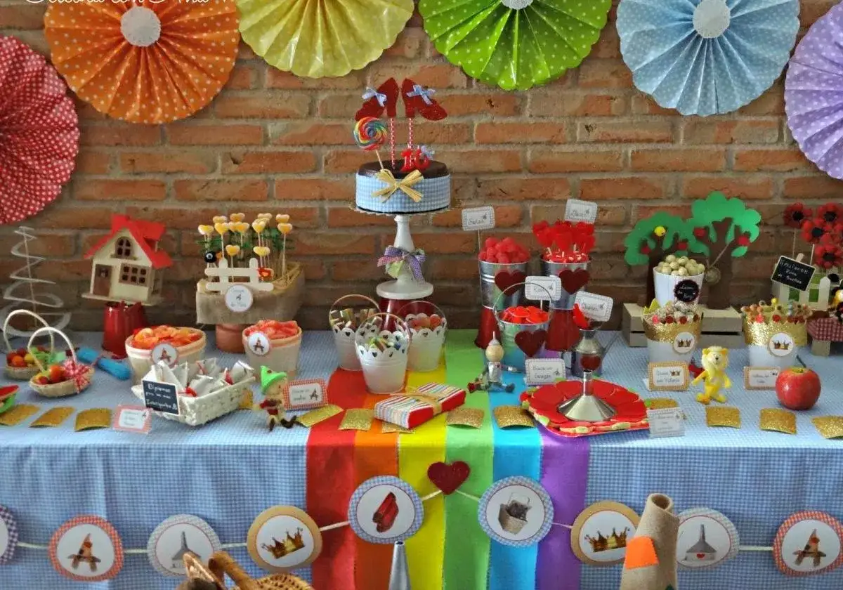 Mesa llena de centros de chuches para niños, con un pastel decorado, dulces, frutas y adornos temáticos.