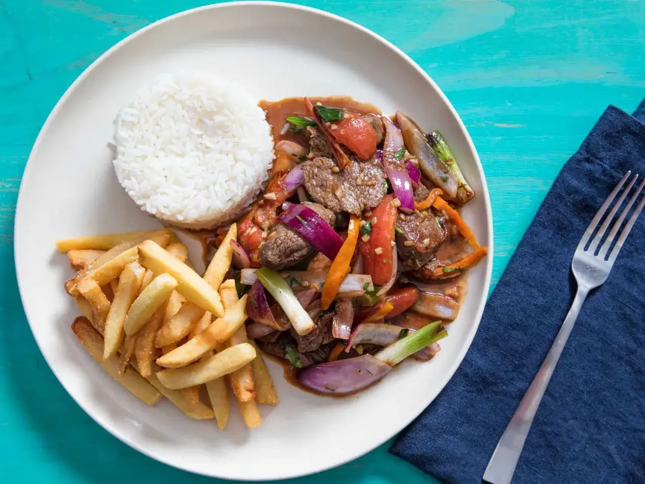 Lomo Saltado: Rindfleischstreifen mit Tomaten, Zwiebeln und Fr&uuml;hlingszwiebeln, serviert mit Reis und Pommes Frites.