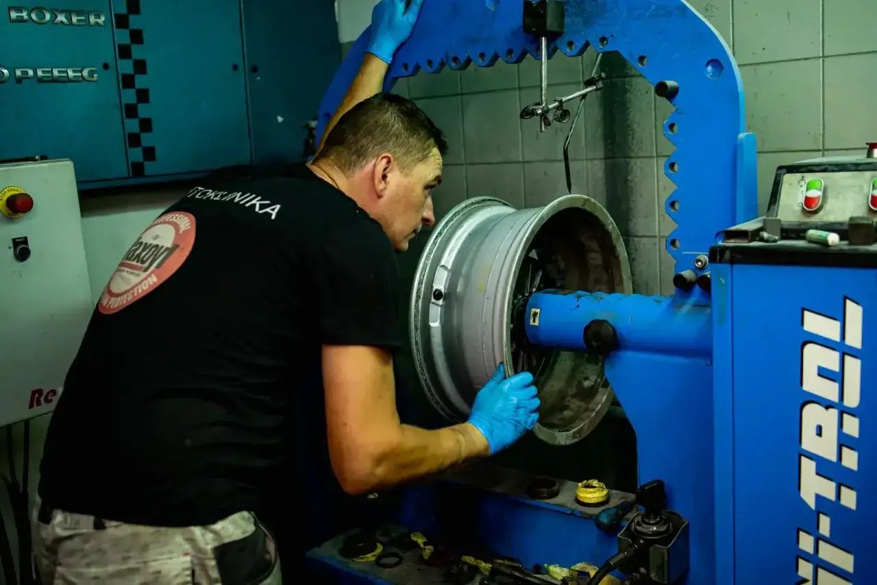 Mechanik w niebieskich rękawiczkach dokonuje precyzyjnego prostowania felgi aluminiowej na specjalistycznej maszynie.