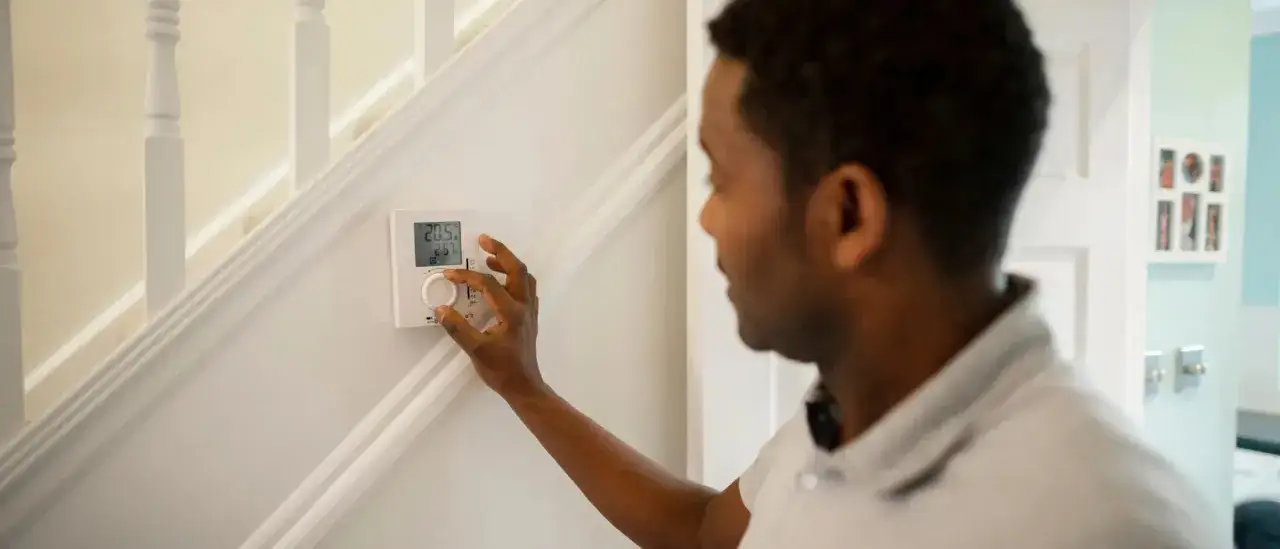Un homme ajuste le thermostat connecté de son poêle à granulés, affichant 20.5°C.