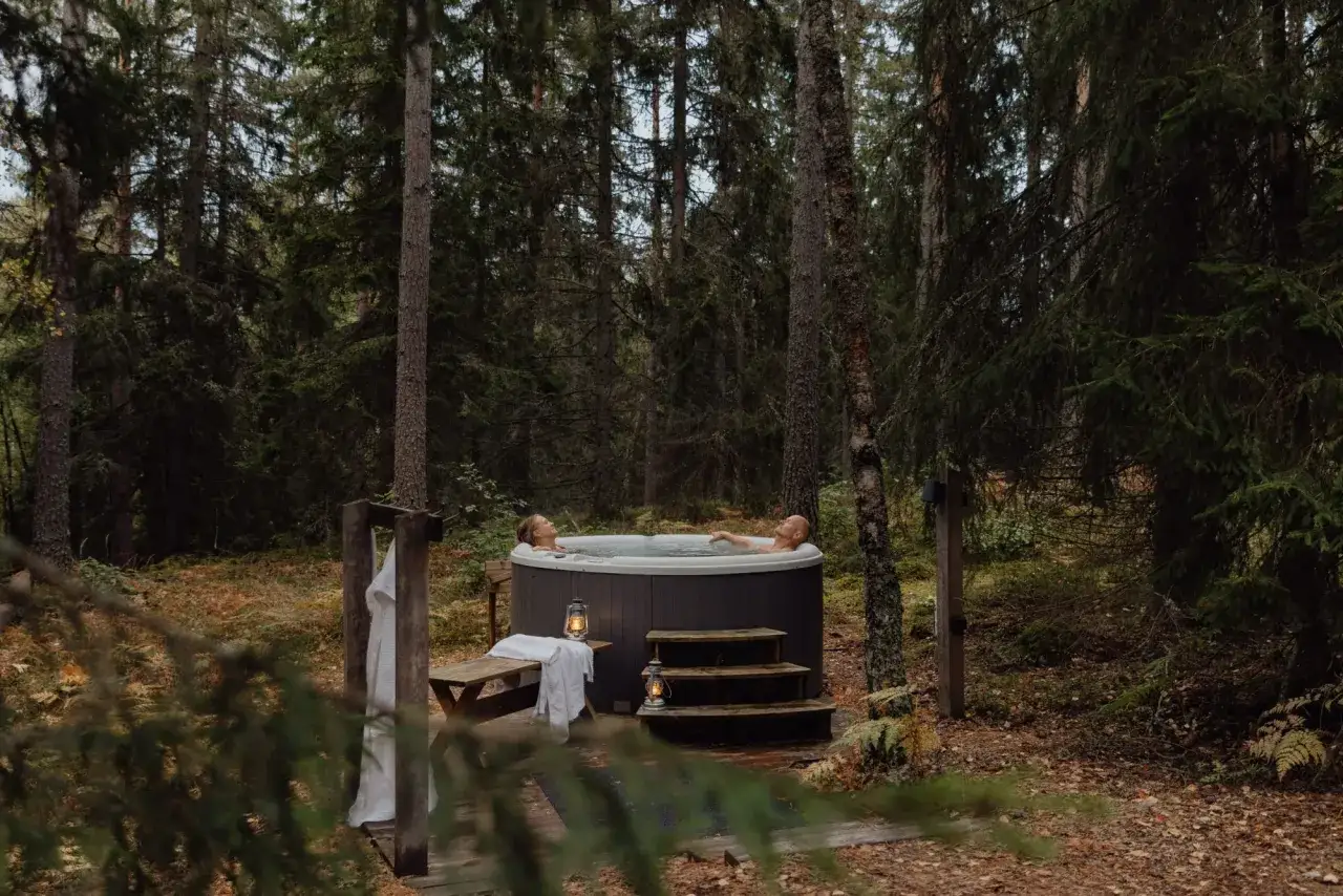 Par njuter av ett bad i en badtunna mitt i en svensk skog. En idyllisk upplevelse av ett naturhotell Sverige.
