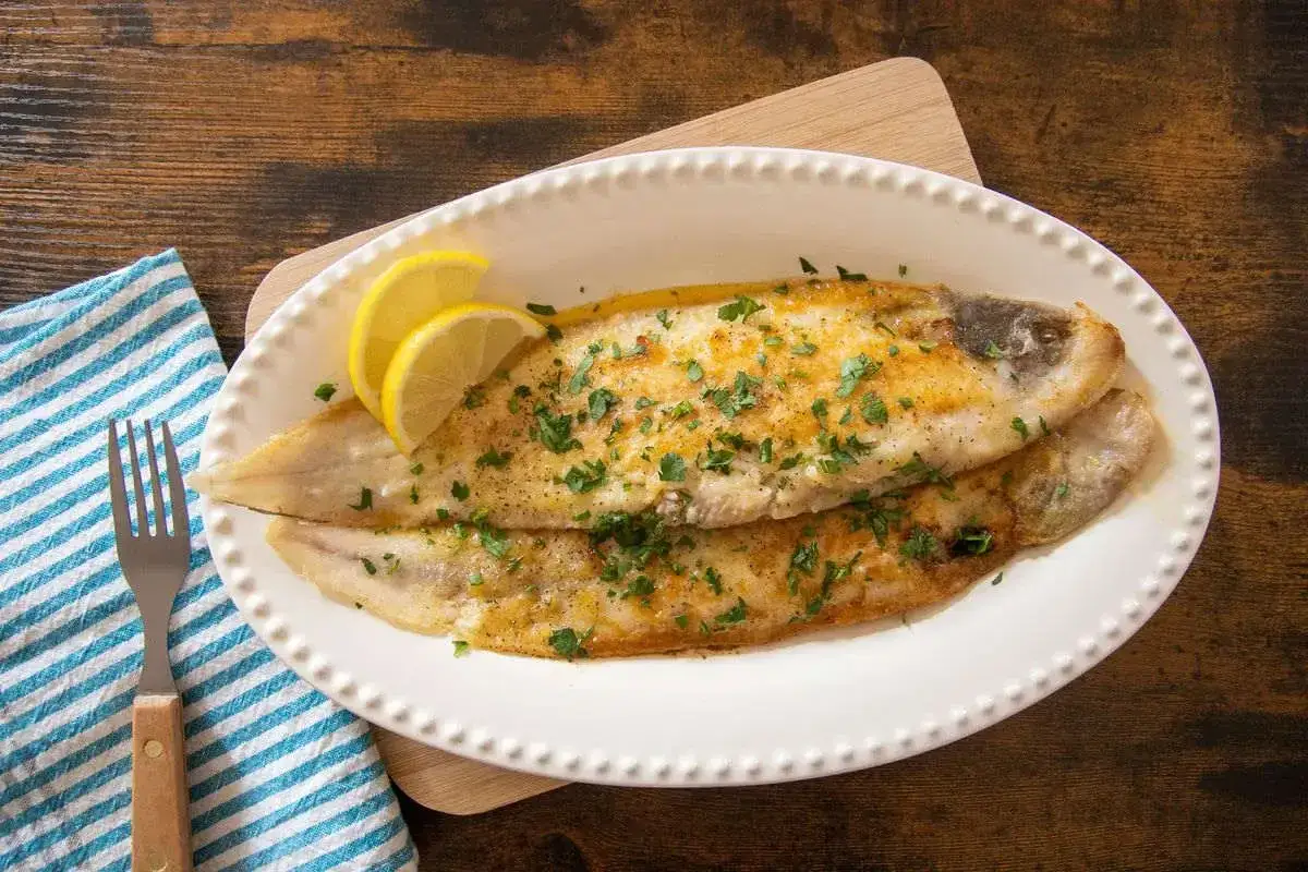 Due sogliole dorate, guarnite con prezzemolo e spicchi di limone, pronte per essere gustate come sogliola alla parmigiana.