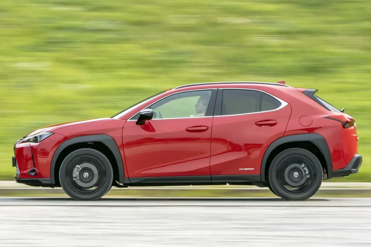 Czerwony Lexus UX w ruchu, z rozmytym zielonym tłem. Idealne **lexus ux wymiary** dla miejskiej dżungli.