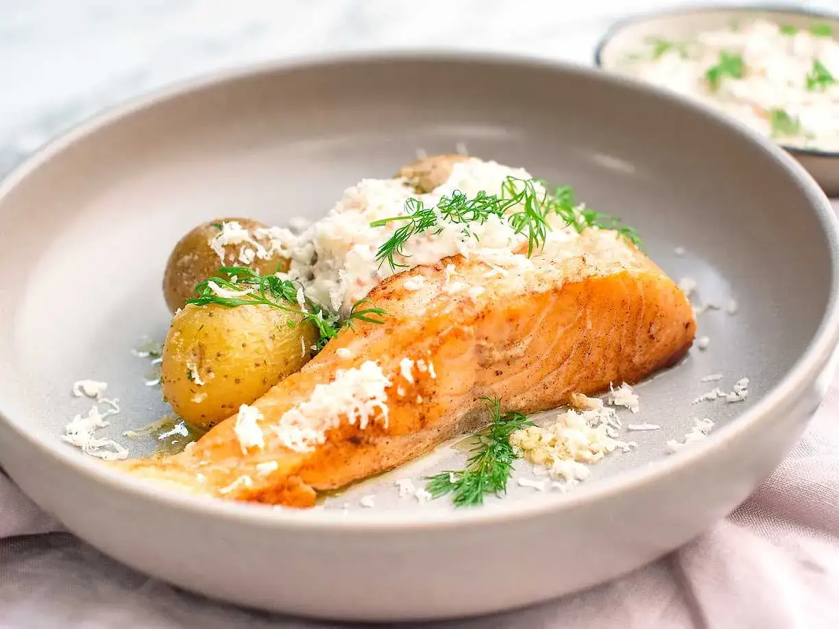 En saftig laxfilé med småpotatis och en krämig romsås till laxen, garnerad med dill och riven ost.