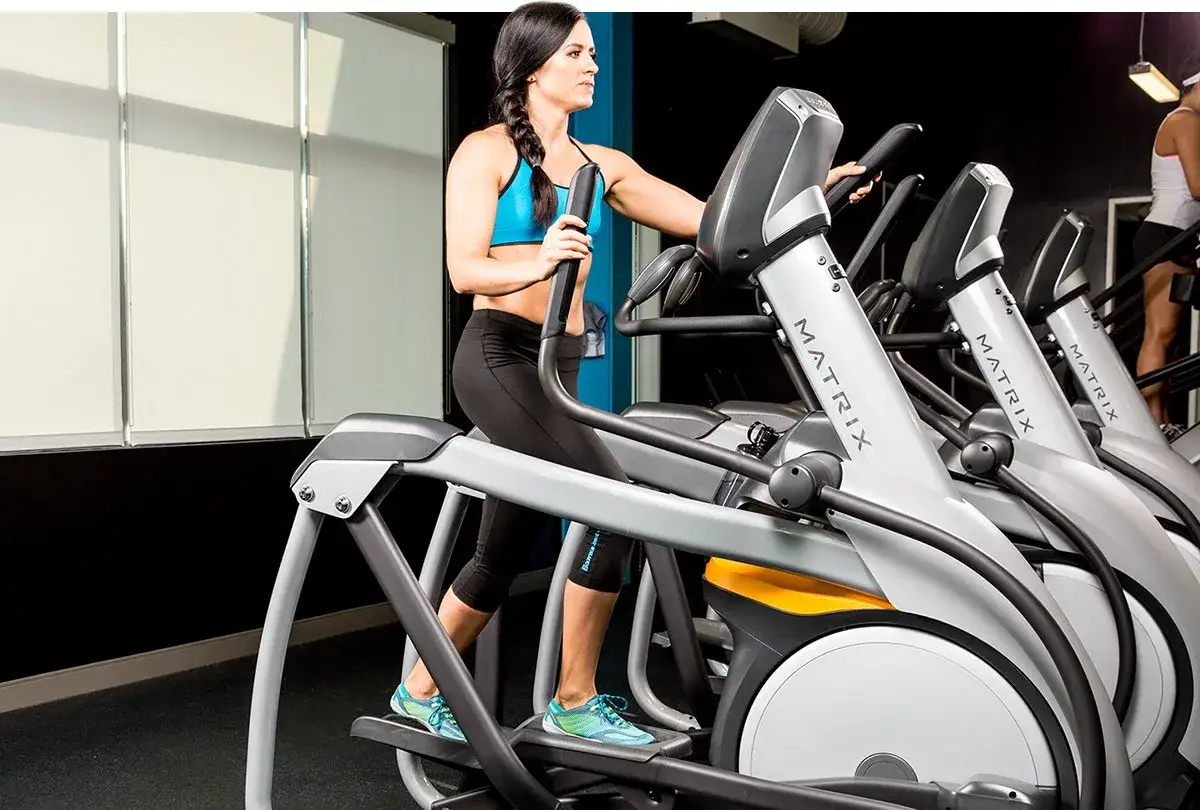 Kobieta wykonuje cardio na siłowni, ćwicząc na orbitreku.