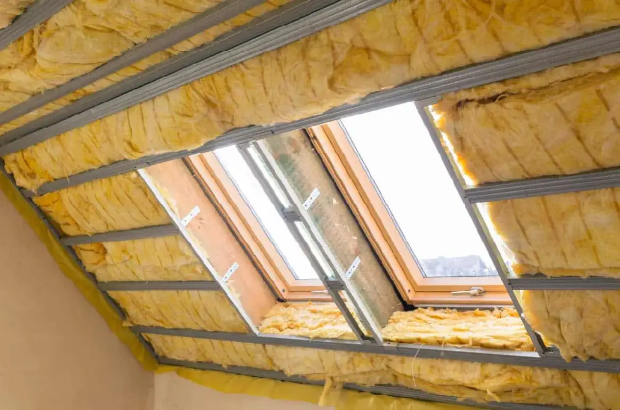 Isolation de toiture en laine de verre, avec structure métallique et pare-pluie jaune visible. Des fenêtres de toit sont installées.