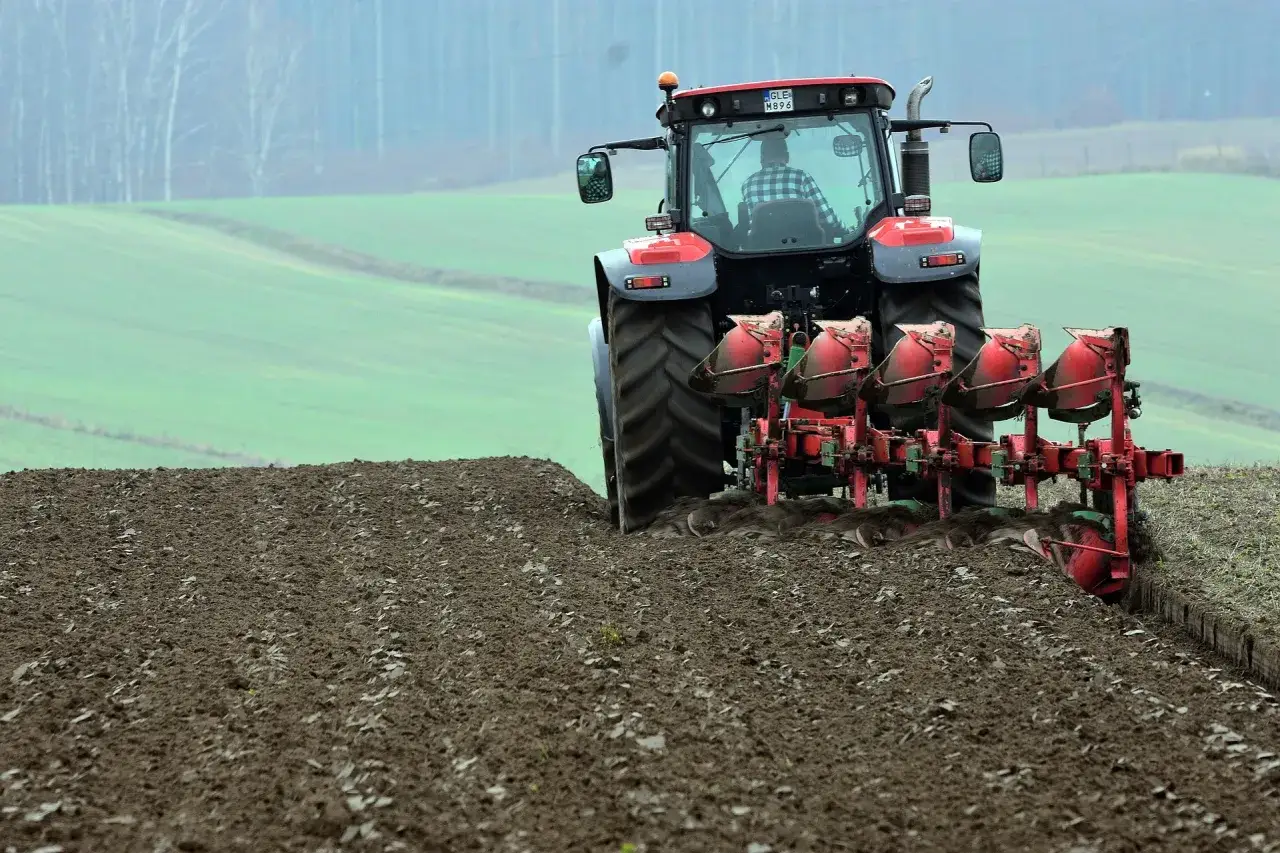 Czerwony traktor z wieloskibowym pługiem do orania pracuje na polu, przygotowując ziemię pod zasiew.