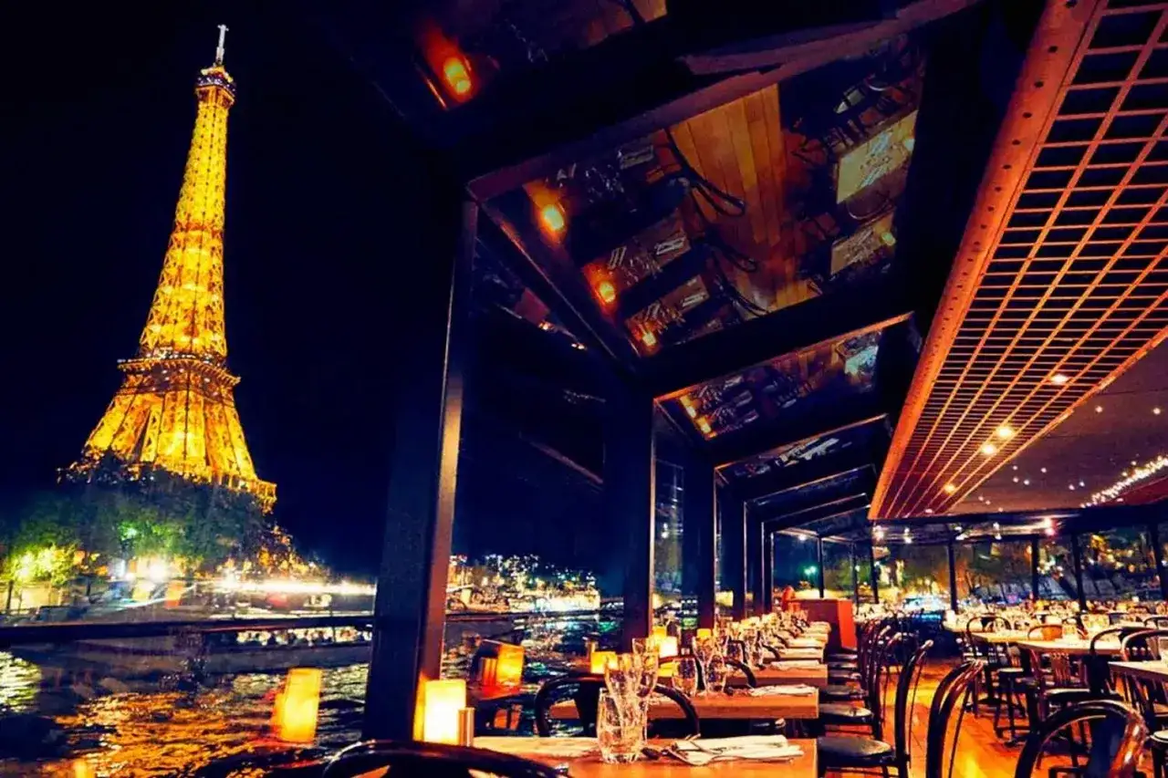 Dîner romantique dans un restaurant sur Seine à Paris, avec la Tour Eiffel illuminée en arrière-plan.