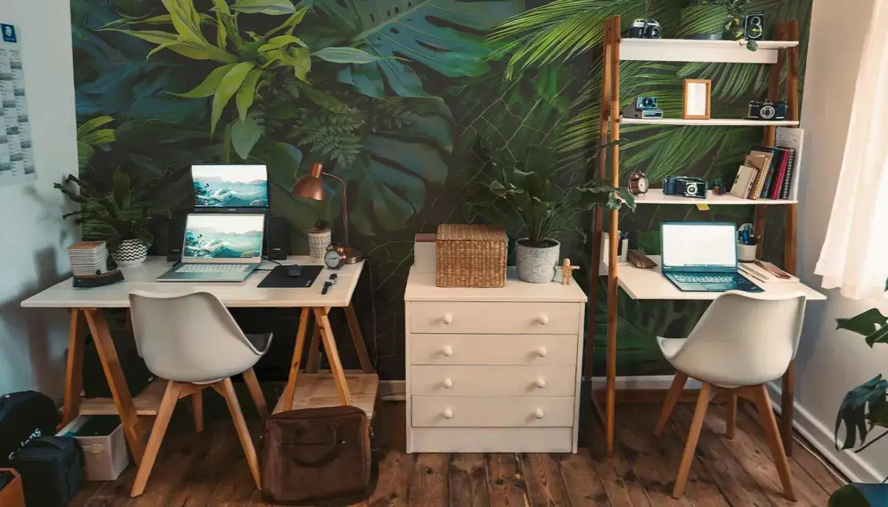 Un bureau chaleureux avec un mur v&eacute;g&eacute;tal luxuriant, deux postes de travail &eacute;quip&eacute;s d'ordinateurs portables, une &eacute;tag&egrave;re remplie d'objets d&eacute;coratifs et de livres.