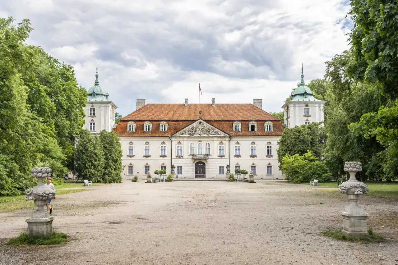 Pałac w Nieborowie, z charakterystycznymi wieżyczkami i ceglanym dachem, otoczony zielenią.