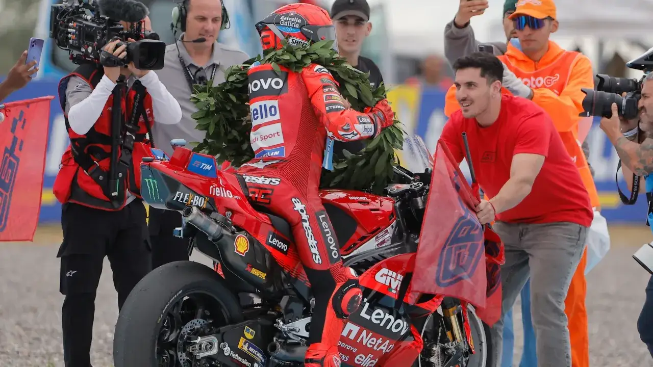 Piloto de MotoGP con casco y traje rojo, rodeado de laureles y una moto Ducati. Se pregunta cuanto mide Marc M&aacute;rquez.