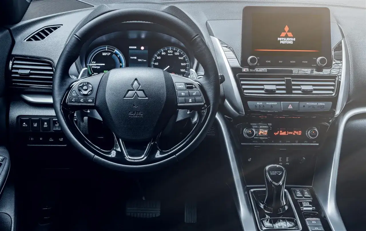 Wnętrze Mitsubishi Eclipse Cross. Kierownica, ekran multimediów z logo Mitsubishi Motors. Opinie o tym aucie są różne, ale wnętrze wygląda nowocześnie.