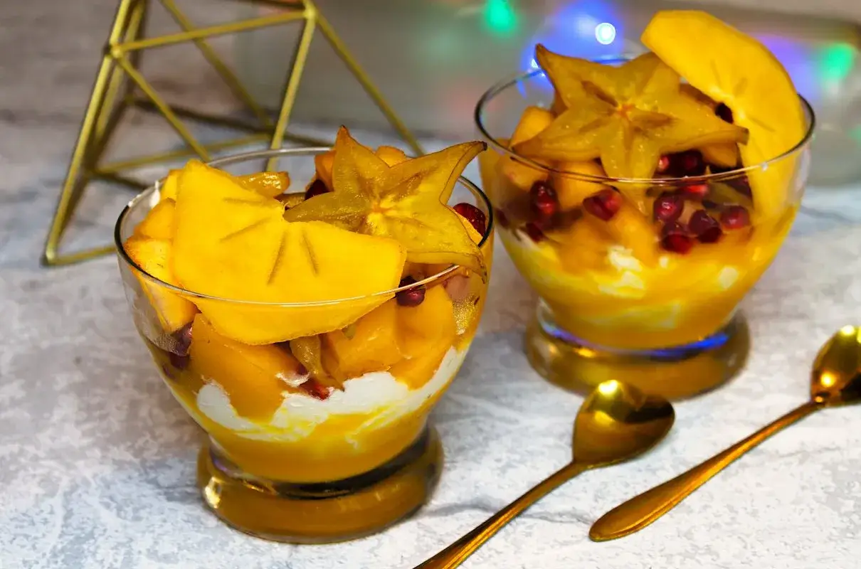 Słodka kasza bulgur z mango, karambolą i granatem w pucharkach. Złote łyżeczki czekają na deser.