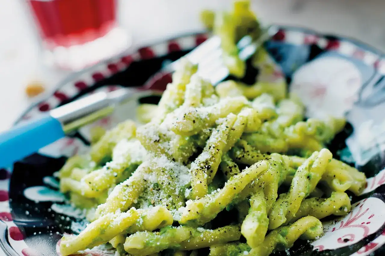 En portion strozzapreti pasta med gr&ouml;n s&aring;s och riven ost, redo att avnjutas med en gaffel.
