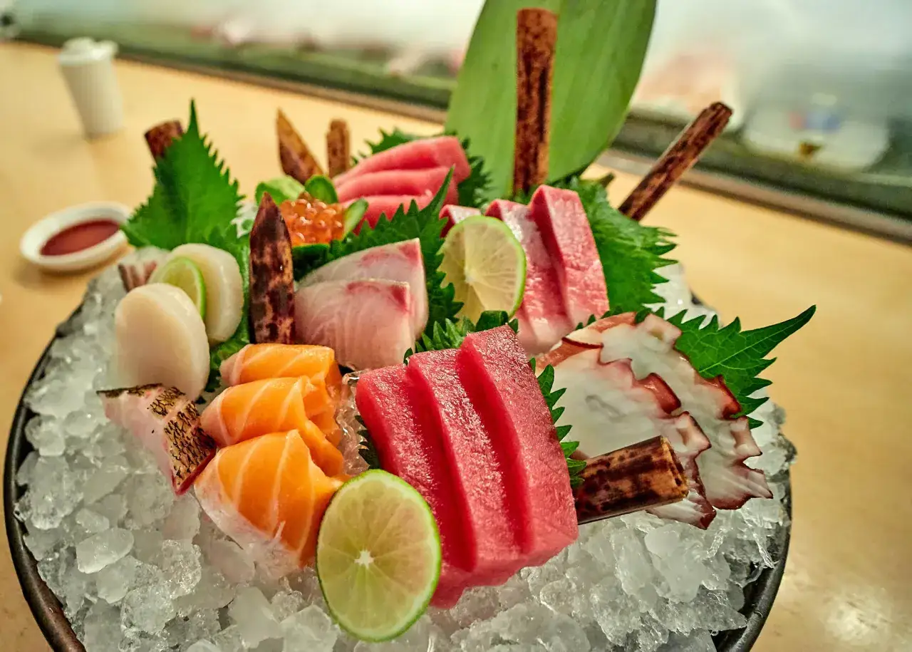 Sashimi-Platte mit Lachs, Thunfisch, Jakobsmuscheln und Oktopus auf Eis, garniert mit Limettenscheiben und Bl&auml;ttern.