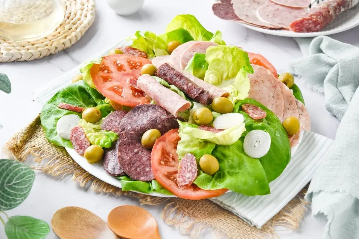 Una generosa ensalada catalana con lechuga, tomate, aceitunas, cebolla y una variedad de embutidos y fiambres.