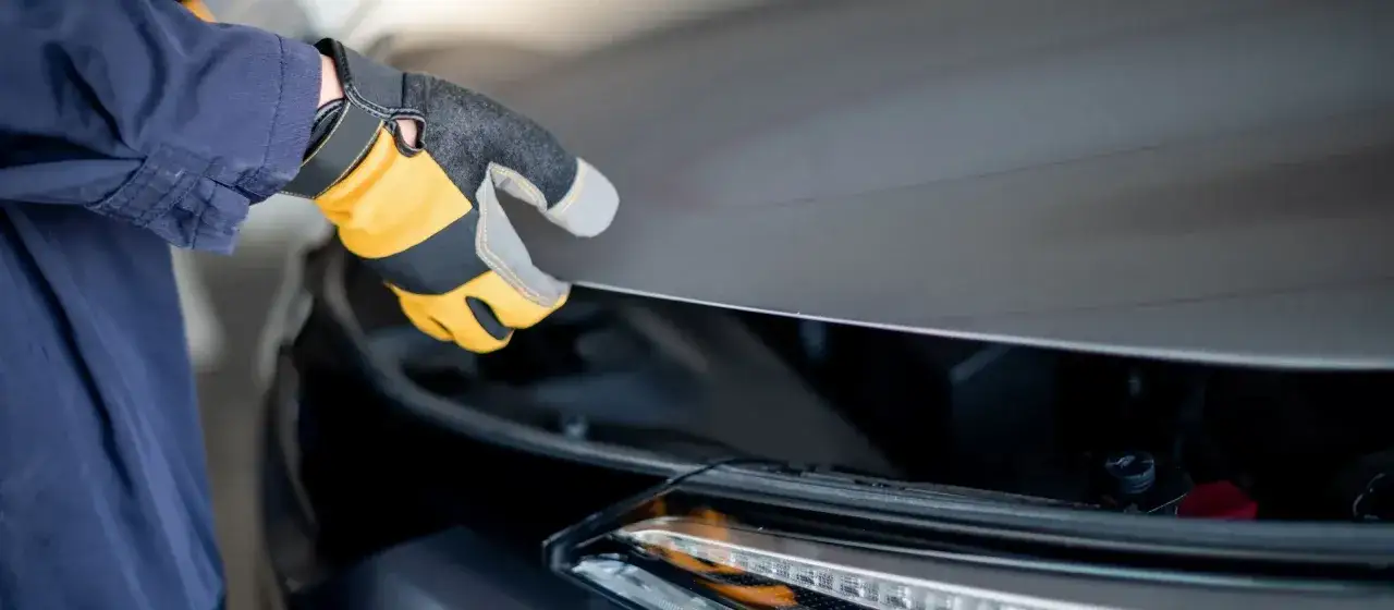 Ręka w rękawicy zamyka maskę samochodu. Co jeśli samoch&oacute;d nie przejdzie przeglądu? Czas na wizytę u mechanika.
