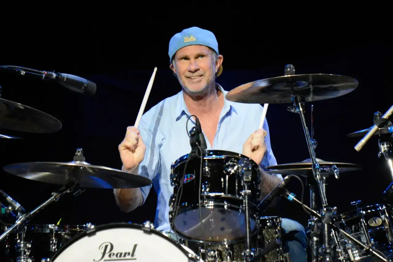 Chad Smith z zespołu Red Hot Chili Peppers gra na perkusji, ubrany w błękitną koszulę i czapkę z daszkiem.