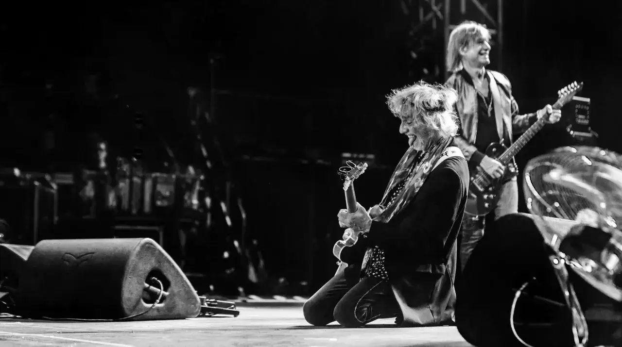 Un groupe rock fran&ccedil;ais des ann&eacute;es 2000 en pleine performance. Le guitariste principal, &agrave; genoux, exprime sa passion avec sa langue tir&eacute;e.