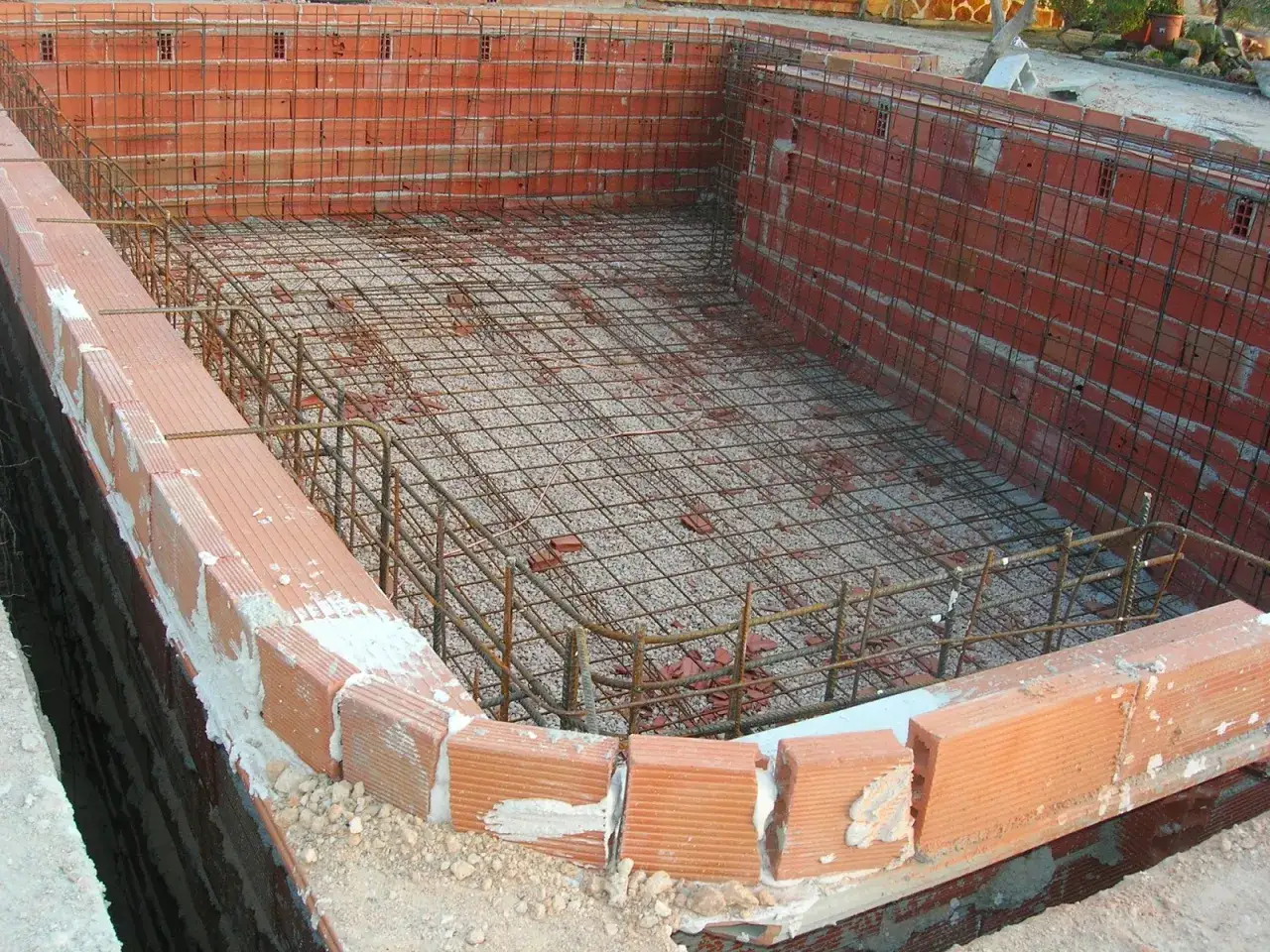 Construcción de una piscina de obra: paredes de ladrillo y armadura de hierro listas para el hormigón.