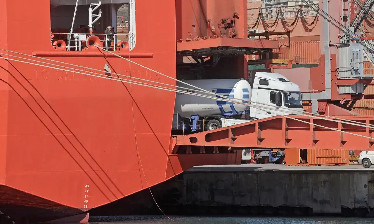 Ein wei&szlig;er Tanklastwagen wird per **roll on roll off** in einen gro&szlig;en roten Frachter geladen.