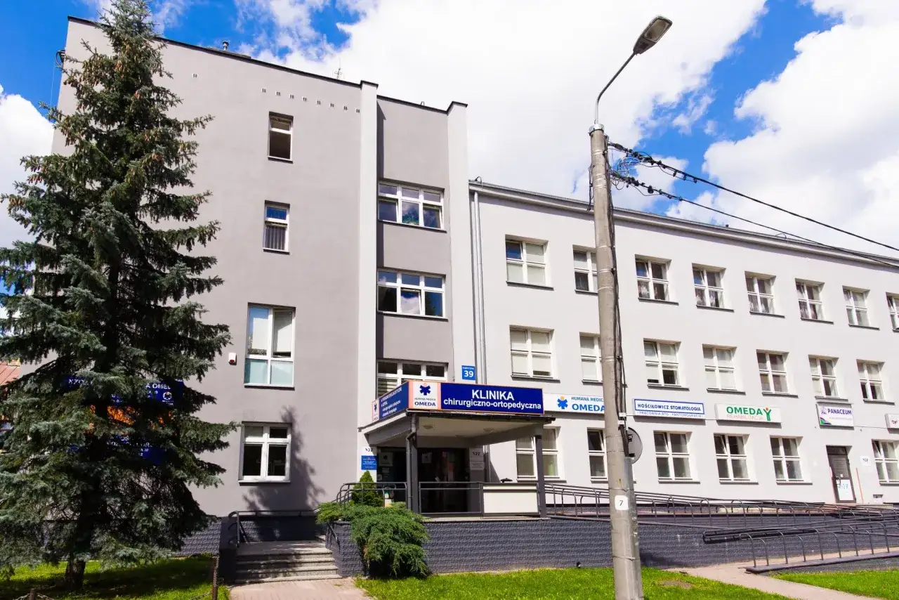 Budynek kliniki chirurgiczno-ortopedycznej OMEDA w Białymstoku z drzewem i niebieskim niebem.