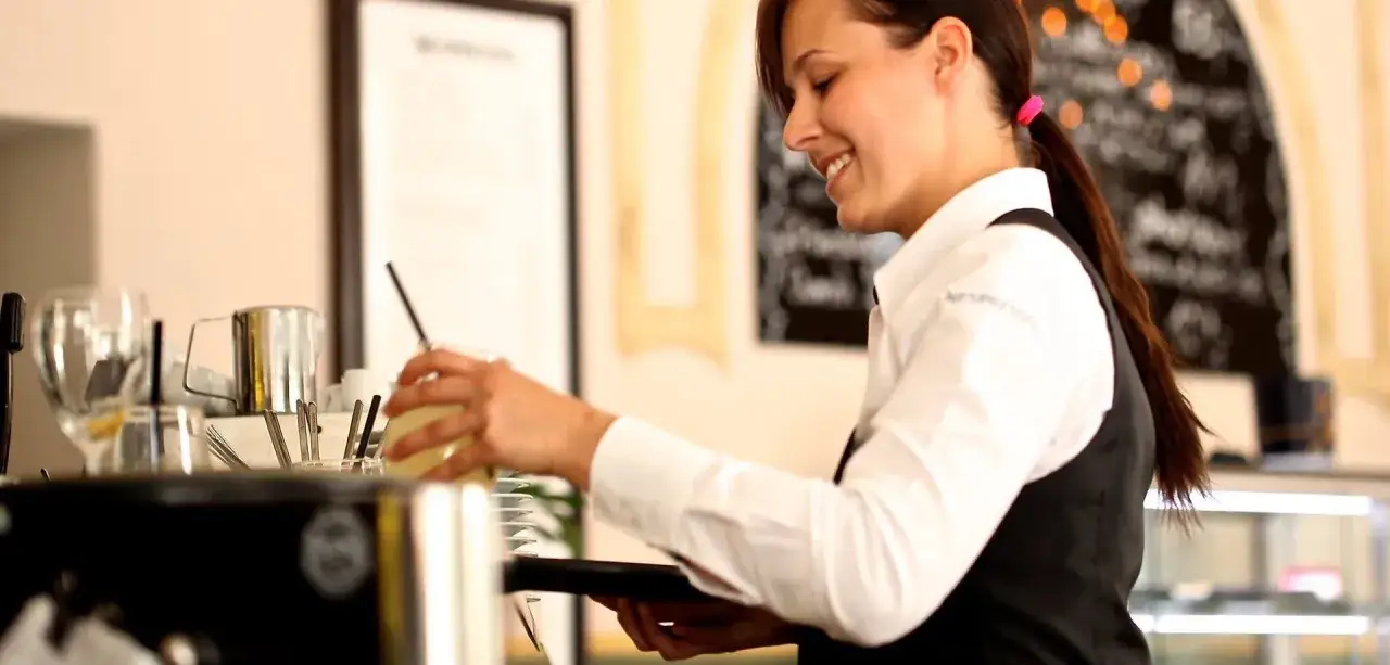 Camarera sonriente prepara bebida. Un tpv hosteler&iacute;a que es, es un sistema para gestionar pedidos y pagos en restaurantes.