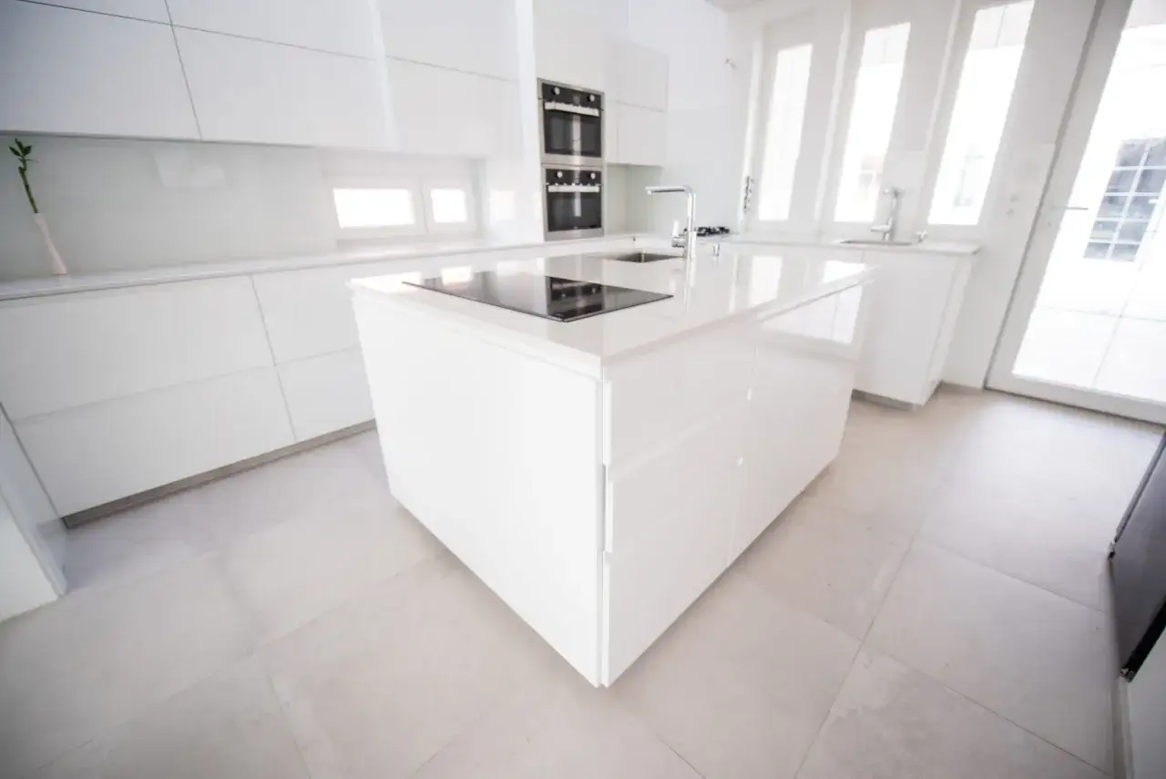 Isola centrale con piano cottura e lavello in una moderna cucina laccata lucida. Ante a filo e finiture minimaliste.