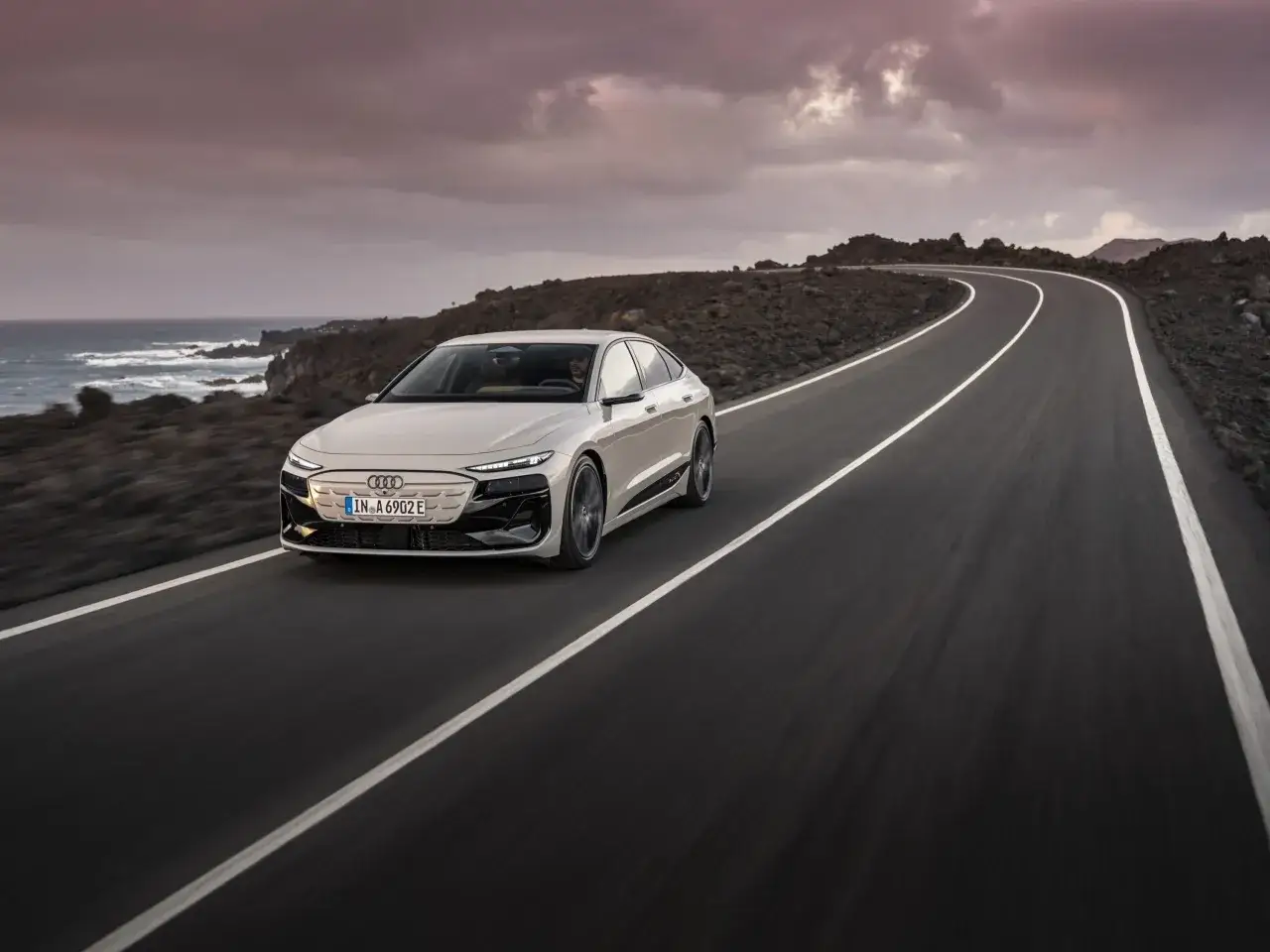 Białe Audi A6 e-tron sunie po krętej drodze nad oceanem.