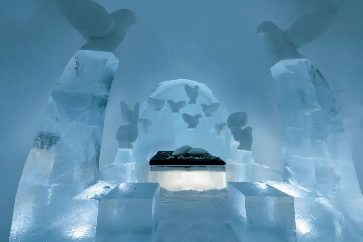 Vacker ishall med iskonst i form av duvor. En säng med kuddar står i mitten. Ett magiskt igloo hotell Sverige.