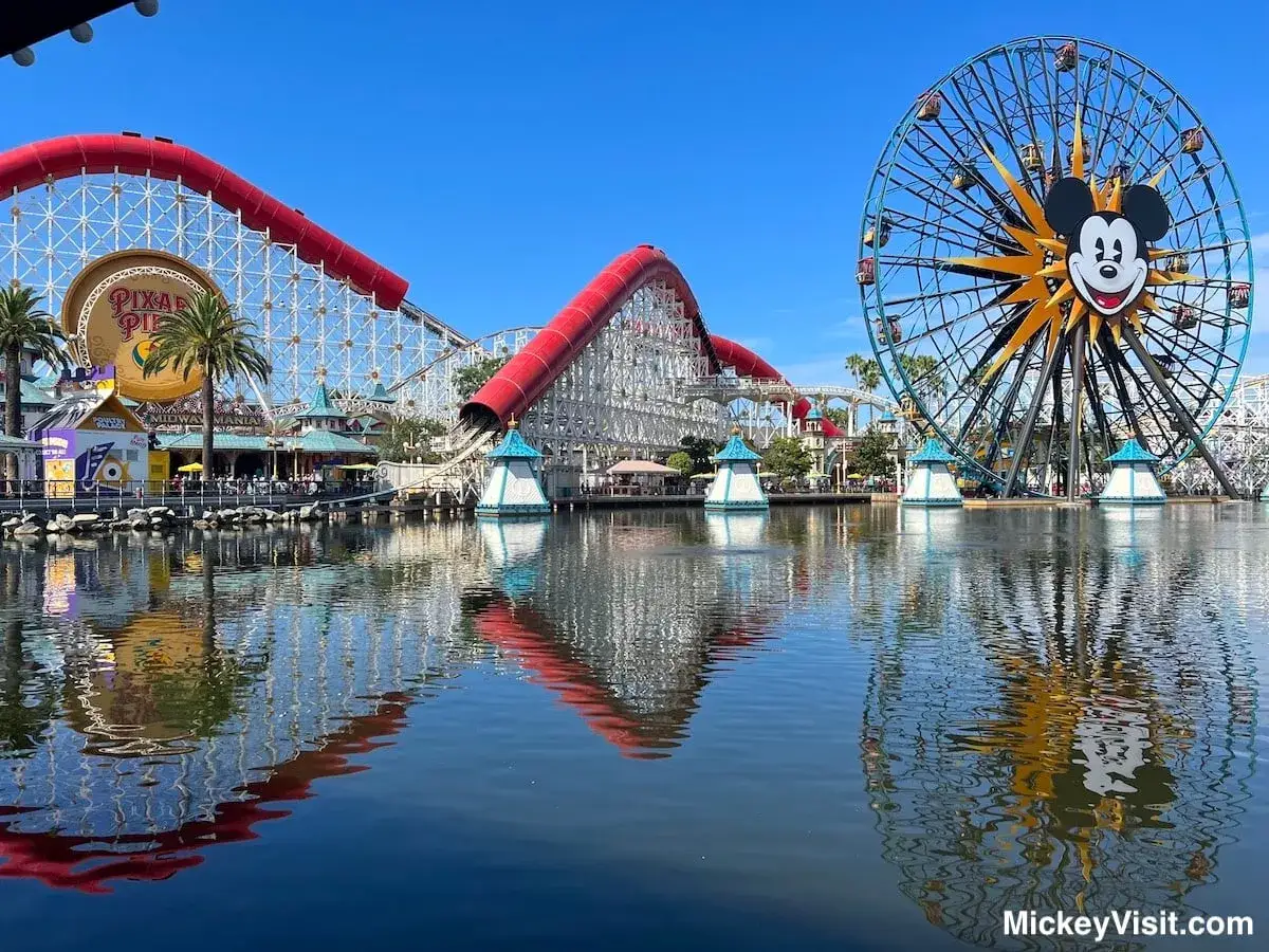 Widok na park rozrywki Disneyland z diabelskim młynem i kolejką górską odbijającymi się w wodzie.
