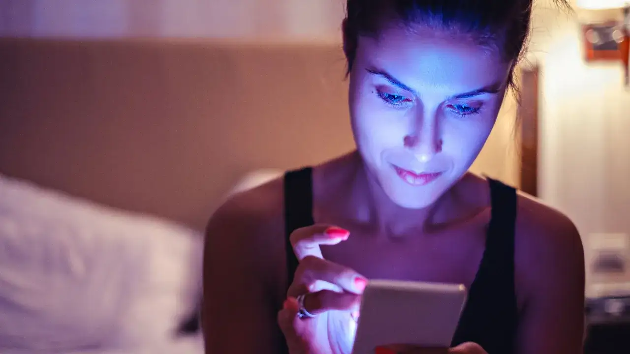 Mujer absorta en su móvil, iluminada por la luz azul. ¿Qué es la luz azul? Es la que emiten las pantallas, afectando nuestro sueño.