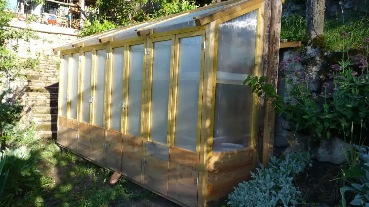 Une serre pour semis fait maison, en bois et plastique, abrite des plantes dans un jardin verdoyant.