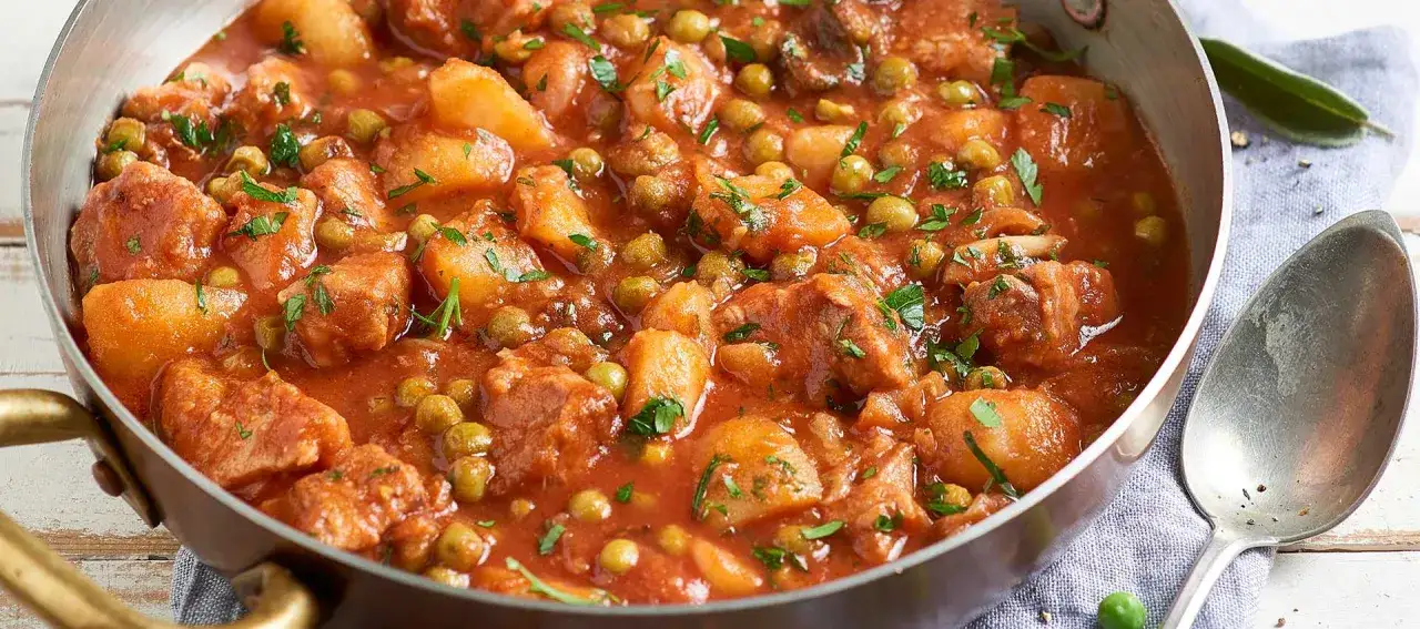 Un saporito spezzatino di vitello con piselli e patate, cotto in un ricco sugo di pomodoro e guarnito con prezzemolo fresco.