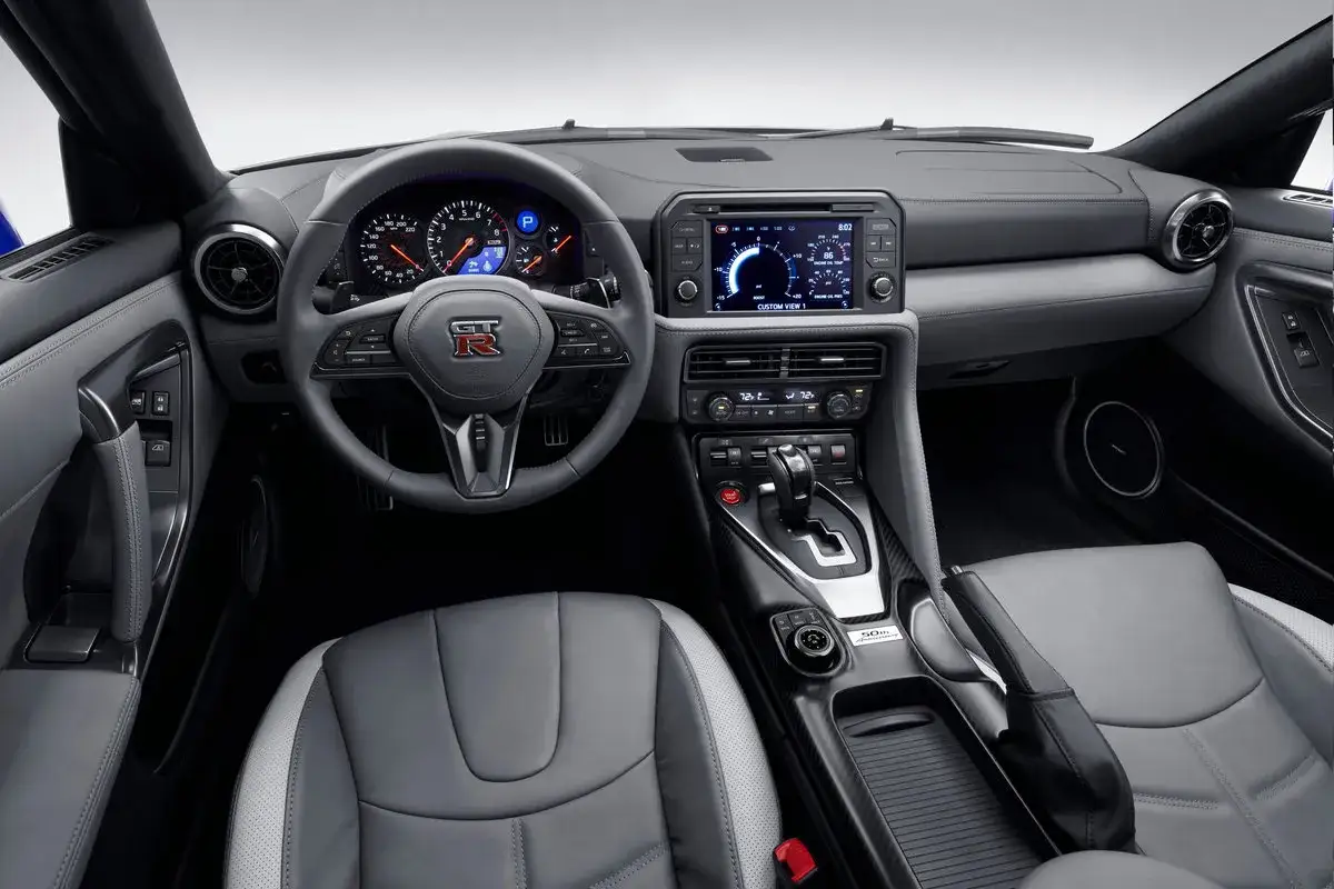 Wnętrze Nissan R35 GT-R z szarymi skórzanymi fotelami, kierownicą z logo GT-R i ekranem multimedialnym.