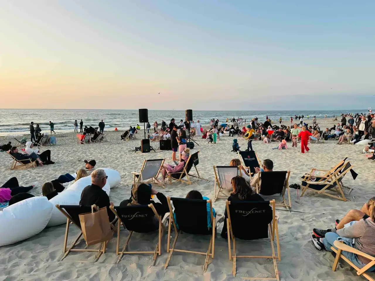 Wieczorne **krynica morska imprezy na plaży** z muzyką na żywo. Ludzie siedzą na leżakach, relaksując się przy zachodzie słońca.