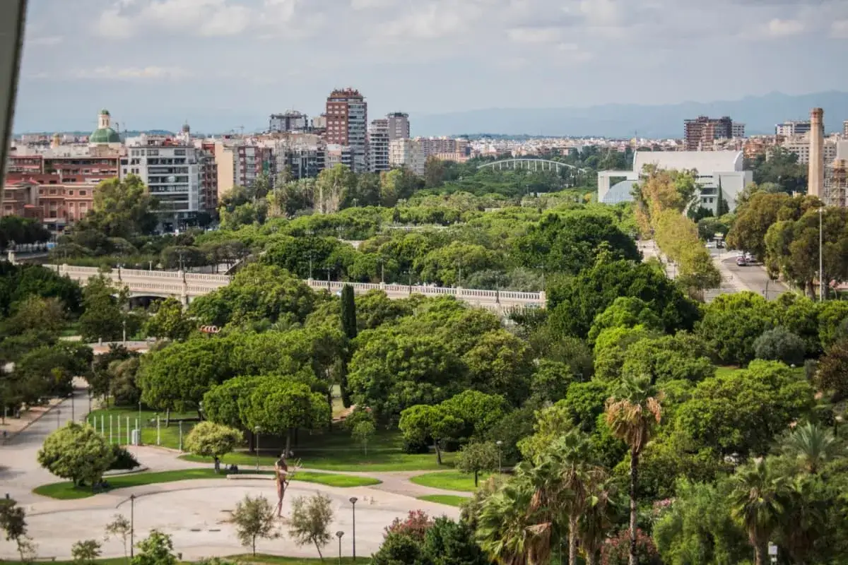 Un paesaggio urbano verdeggiante con edifici sullo sfondo, un parco rigoglioso e un ponte, che incarna il **goal 11 agenda 2030** per città sostenibili.