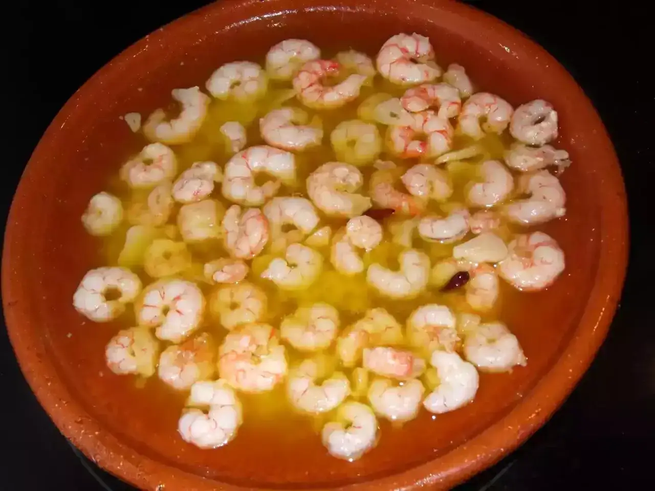 Gambas al ajillo receta: jugosas gambas cocinándose en aceite de oliva con ajo y guindilla en una cazuela de barro.