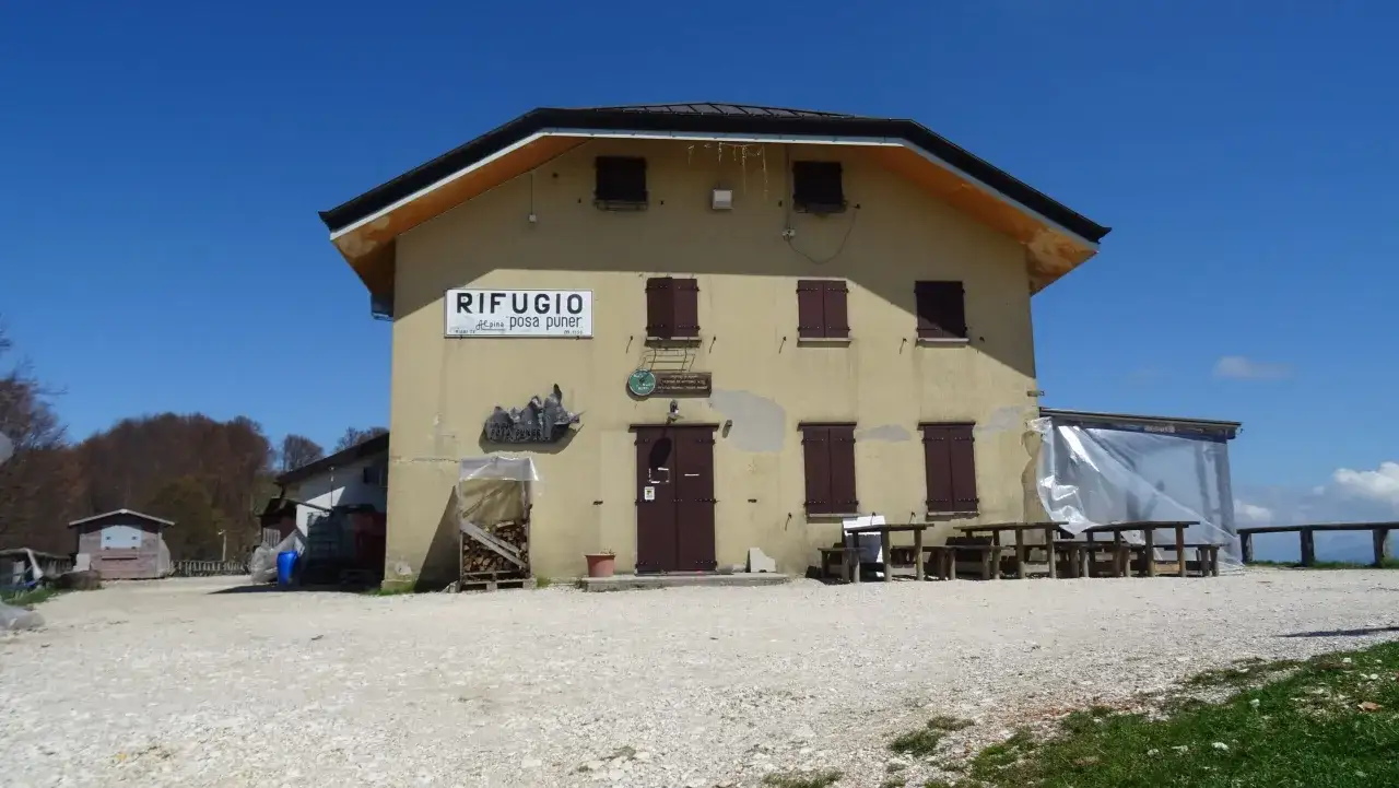 Rifugio Posa Puner, un edificio giallo con finestre marroni e un cartello che indica il nome, sotto un cielo azzurro.