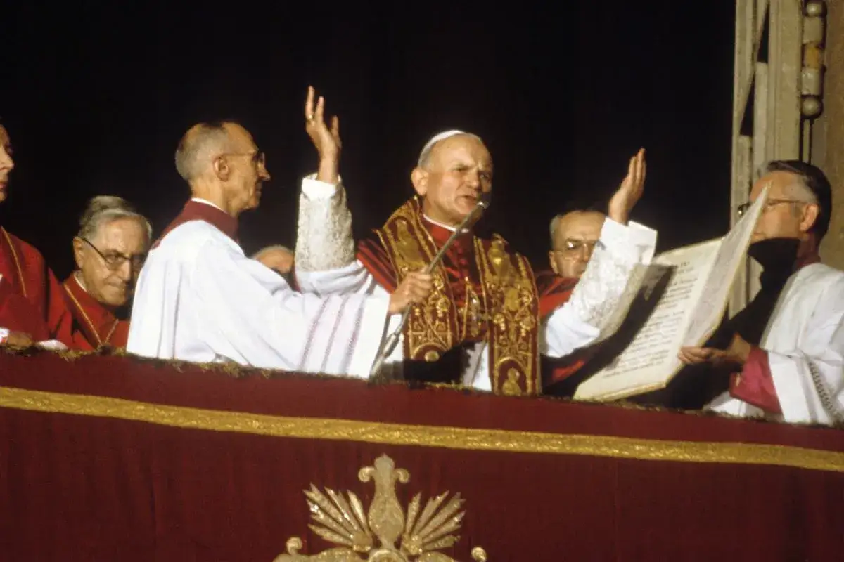 Papież Jan Paweł II przemawia do wiernych, otoczony przez duchownych. Jego gesty i słowa mogą być interpretowane w senniku.