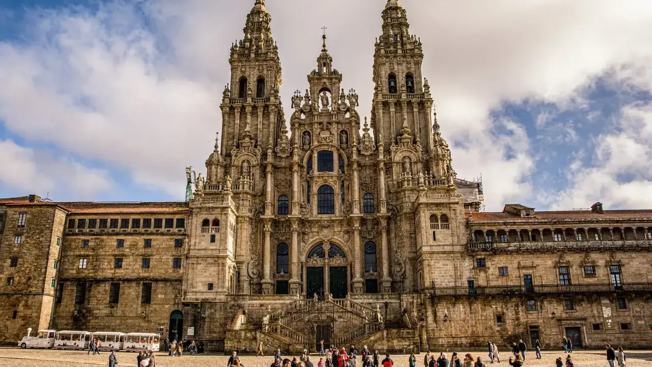 Majestuosa fachada de catedrales barrocas, con escalinatas y torres imponentes bajo un cielo nublado. Turistas pasean por la plaza.